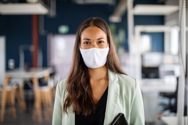 Portrait of a businesswoman with face mask in office Close-up portrait of a businesswoman with face mask in office. Woman with protective face mask standing in office and looking at camera. reopening photos stock pictures, royalty-free photos & images