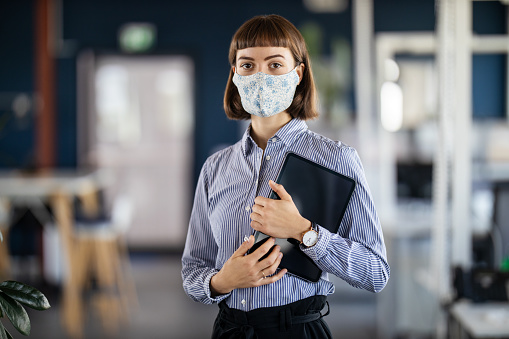 Portrait of a young businesswoman with short blond hair wearing face mask in office. Businesswoman in office with her digital tablet.