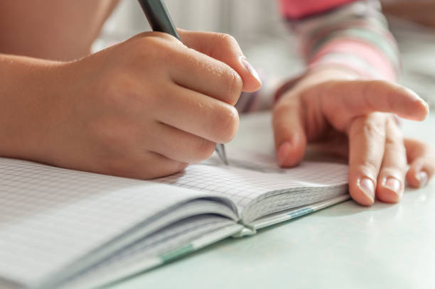 istock children's hands hold the pen. Children writes something in a notebook 1264983049