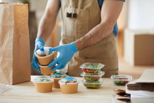 Worker Wearing Gloves at Food Delivery Service Closeup of unrecognizable worker wearing protective gloves packaging orders at wooden table in food delivery service, copy space take out food photos stock pictures, royalty-free photos & images
