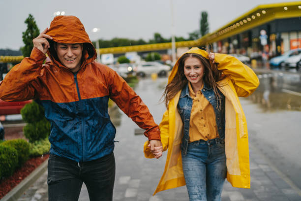 couples heureux exécutant dans la ville un jour pluvieux - courir sous la pluie photos et images de collection