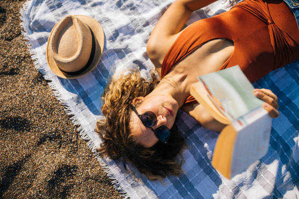 Woman lies on the beach reading a book Woman lies on the beach reading a book sunbathing stock pictures, royalty-free photos & images