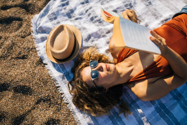 istock Woman lies on the beach reading a book 1264984772
