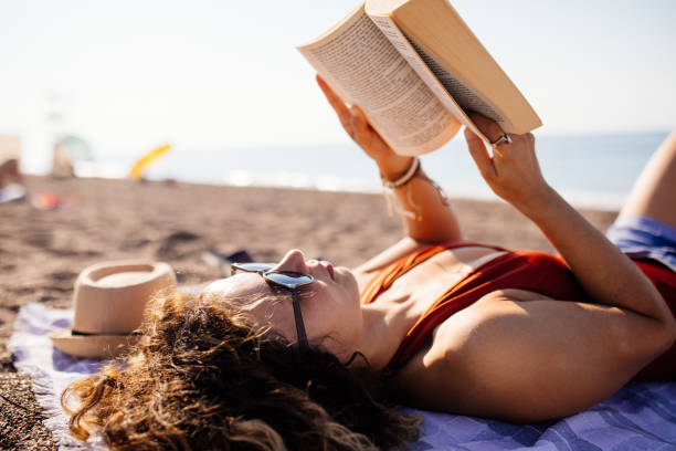 istock Woman lies on the beach reading a book 1264984880