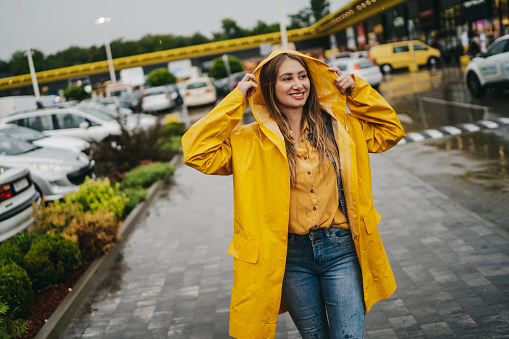 Cheerful young woman in yellow raincoat enjoying rainy weather in the city
