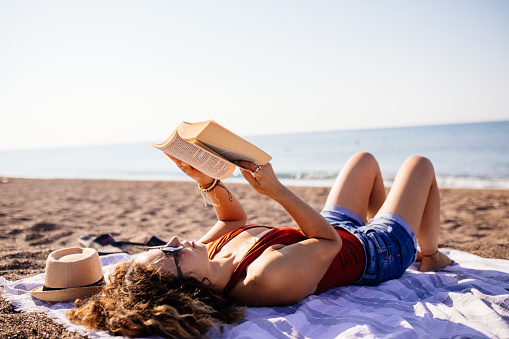 Woman lies on the beach reading a book