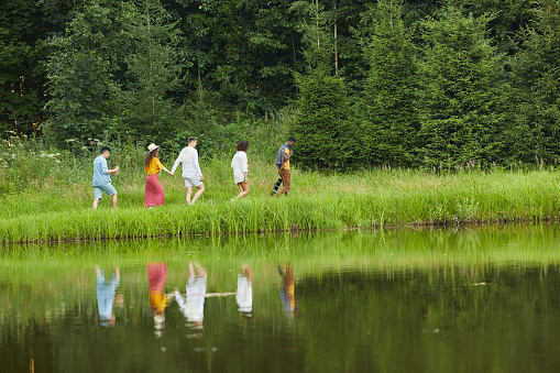 Wide angle view at multi-ethnic group of young people walking by water and enjoying vacation in Summer, copy space