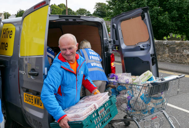 Volunteers unloading a van of food at a community food bank centre 7th August 2020: Volunteers unloading a van of food that has been donated to a charity food bank centre in the town of Penicuik, in Midlothian, Scotland. A man wearing a blue and red coat is carrying a full tray of packaged fresh meat. It will be sorted into emergency food parcels to be given to those in crisis. A problem that has increased since the Covid-19 pandemic, with more people losing jobs and getting into financial difficulty. midlothian scotland stock pictures, royalty-free photos & images