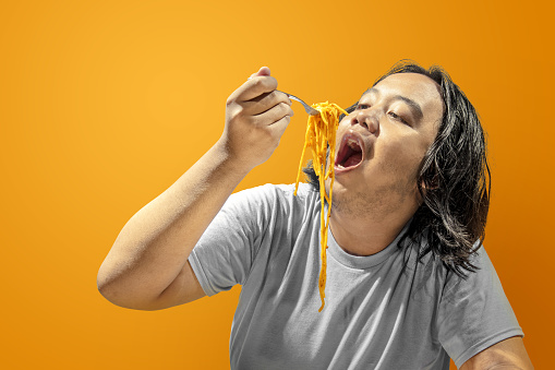 Asian man eating spaghetti with a colored background. Junk food concept