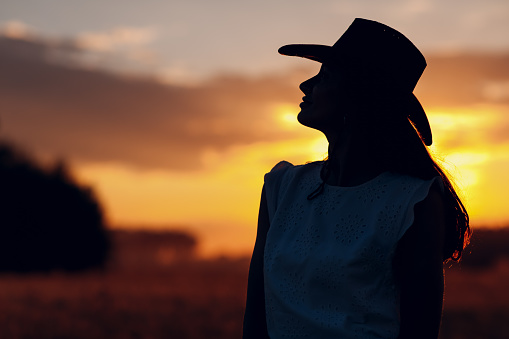 Woman farmer silhouette in cowboy hat at agricultural field on sunset.