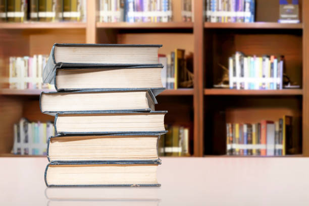 istock Desk with a stack of books with bookshelf background 1264991410