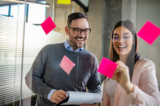 Young creative business people meeting at office. Caucasian businesswoman pointing to a sticky note on glass wall during a brainstorming workshop in office. Young creative business people meeting at office. office fun business adhesive note stock pictures, royalty-free photos & images