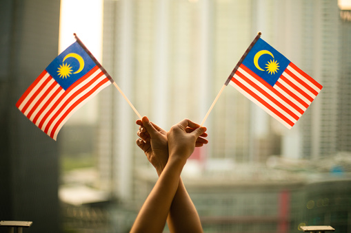 cropped hand of person holding Malaysia Flag in the city scape