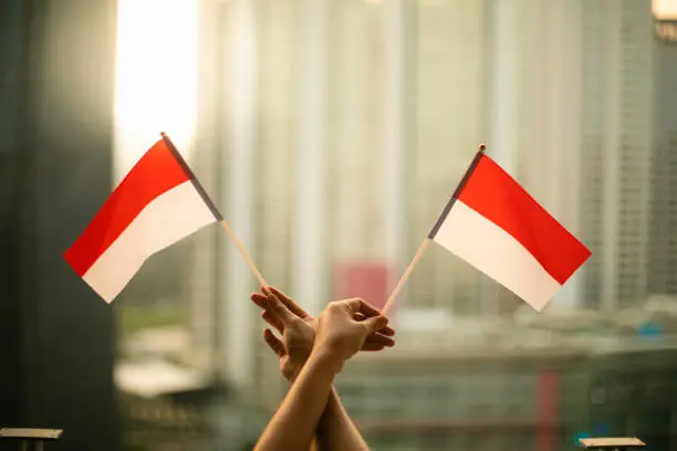 Photo of cropped hand of person holding Indonesia Flag in the city scape