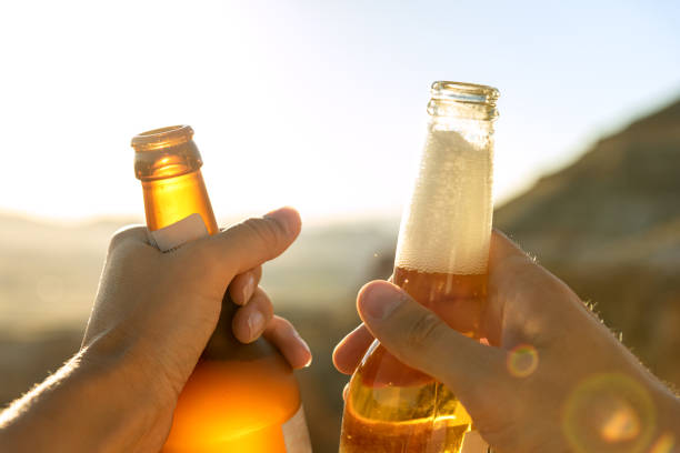 istock Two hands holding bottles with beer against sunset. 1265001192
