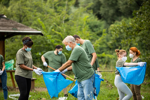 Multi-ethnic group of volunteers cleaning public park during coronavirus pandemic, they are wearing protective face masks