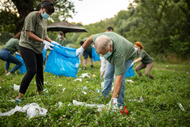volontari che raccolgono rifiuti durante la pulizia del parco pubblico durante la pandemia di covid-19 - bag senior adult outdoors friendship foto e immagini stock