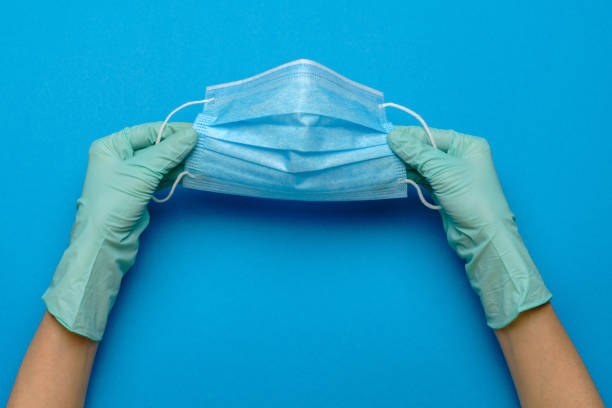 istock Human hand in protective glove holding face protective masks isolated on blue background 1265009950