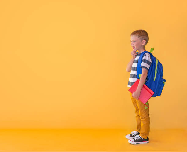 istock A interested boy with book and a backpack looks into the distance on a yellow background. Concept back to school. 1265011252