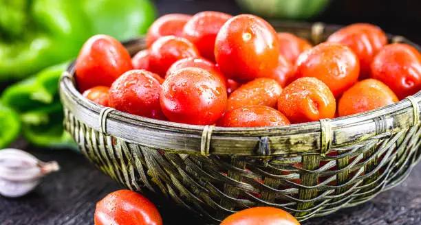 small red tomato, fresh vegetable used in Brazilian cuisine. dark straw basket with organic food