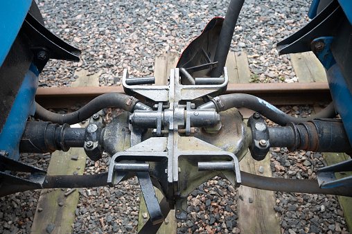A closeup of two old train couplers connected together with railroad tracks and some gravel on the background.