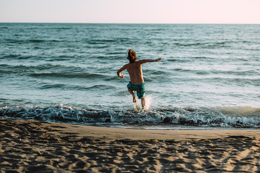 Rear view of a young Caucasian man running toward the sea and jumping in it, relaxing and enjoying his vacation