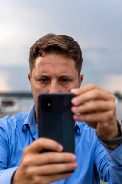 istock Man holding smartphone in his hands at river and taking photographs 1265020497