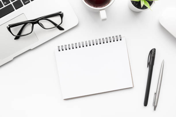istock White office desk table with blank notebook in the middle with pens, laptop computer and supplies. Top view, flat lay. 1265024504