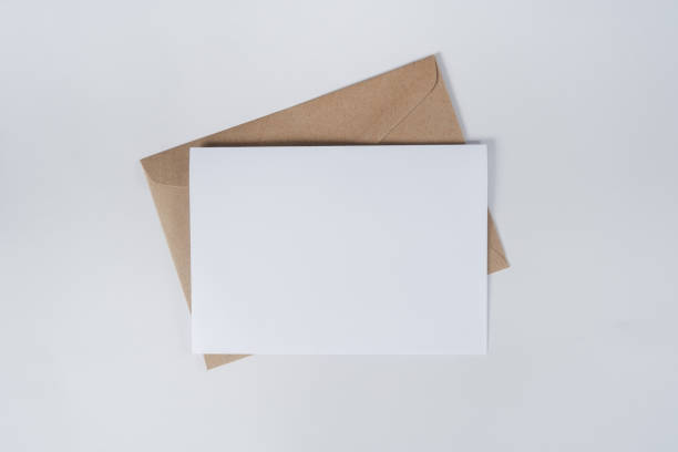 茶色の紙の封筒に白紙が付いている白紙。水平空白グリーティングカードのモックアップ。白い背景にクラフト紙の封筒のトップビュー。文房具のフラットレイ。ミニマリズムスタイル。 - stationary sheet template paper ストックフォトと画像
