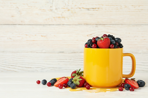 Composition with cup of fresh berries on wooden background, space for text