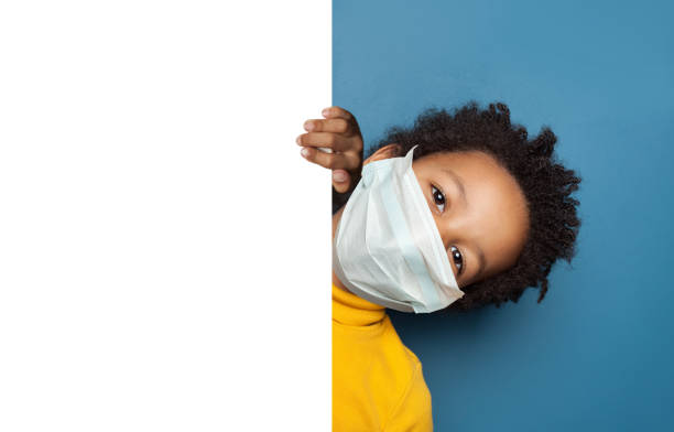 Black child boy in medical protective face mask holding white empty paper singbard Black child boy in medical protective face mask holding white empty paper singbard primary election photos stock pictures, royalty-free photos & images