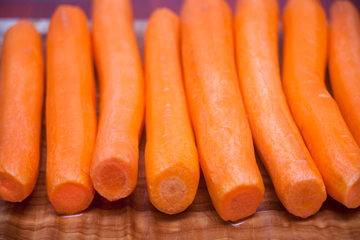 Peeled carrots in a row on wooden cutting board, preparing healthy food. Image suitable for background. Diminishing perspective.