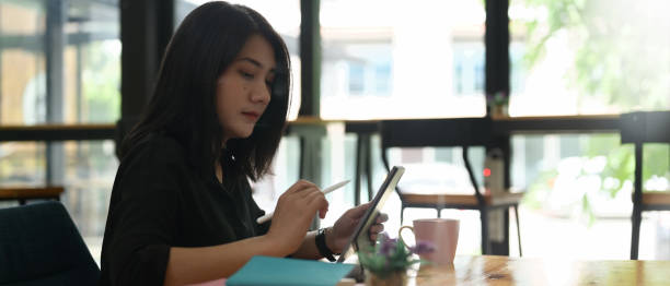 istock A woman is writing on a computer tablet while sitting at the wooden working desk. 1265033641