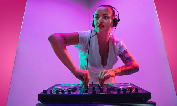 ネオンライトで紫色の背景で演奏ヘッドフォンで若い白人女性ミュージシャン - dj ストックフォトと画像