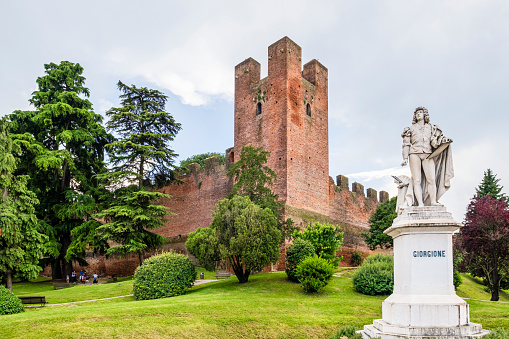 Statue of Giorgione, an Italian Renaissance painter born in Castelfranco Veneto, carved in 1878 by Augusto Benvenuti. In background you can see the town medieval walls. People relaxing in the public park.