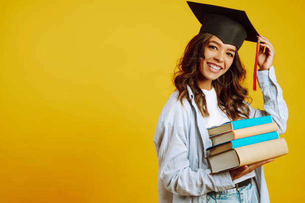 uma mulher graduada com um chapéu de formatura na cabeça, com livros. - graduation student women beauty - fotografias e filmes do acervo