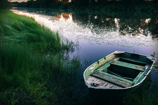Tranquil morning landscape with river bank and old fishing boat at sunrise