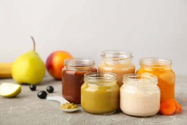 Glass jars with nutrient baby food on grey background Glass jars with nutrient baby food on grey background. Vegetable puree with spoon. baby food stock pictures, royalty-free photos & images