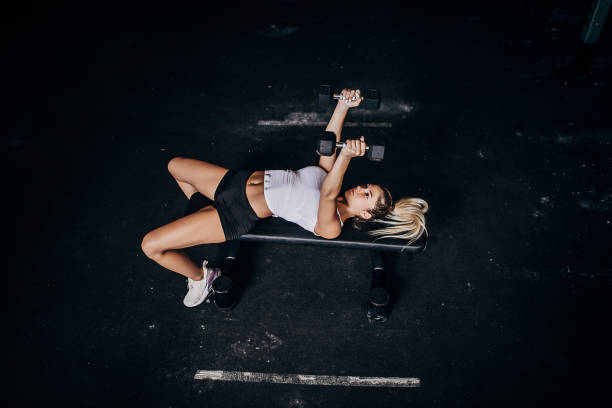 Young sportsman lying on an incline bench, lifting dumbbells with intense focus and determination, dedicated to building strength and enhancing physical fitness during his workout