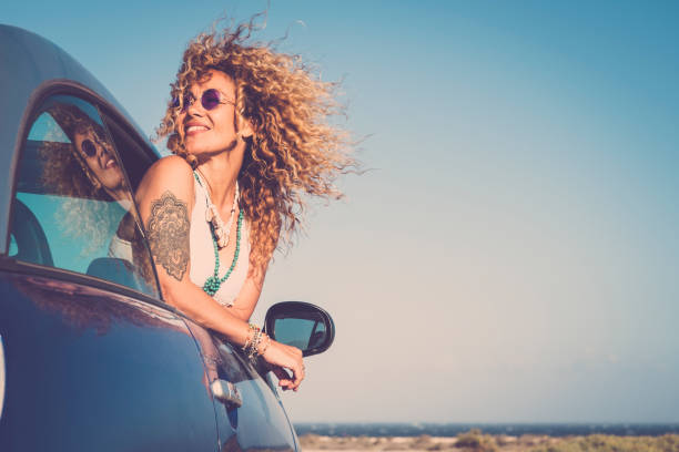 attractive curly blonde young woman smile and enjoy the wind outside the car - concept of beauty and travel for happy and cheerful caucasian people - alternative lifestyle female feel the freedom and joy - female stripper imagens e fotografias de stock