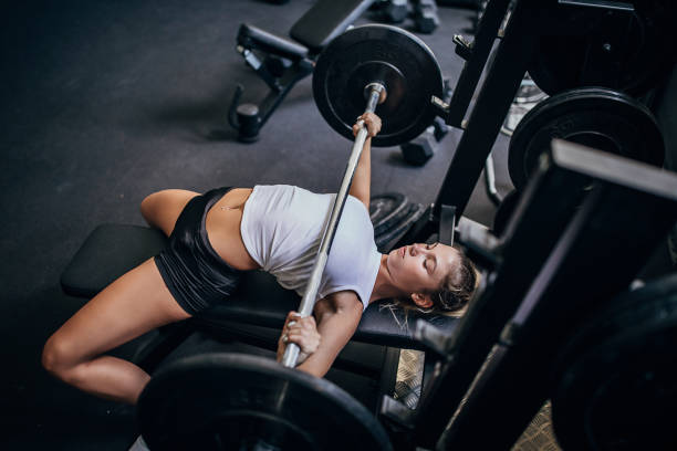 Beautiful young woman bench press training in gym One woman, young blonde woman bench press training in gym alone. blonde female bodybuilders stock pictures, royalty-free photos & images