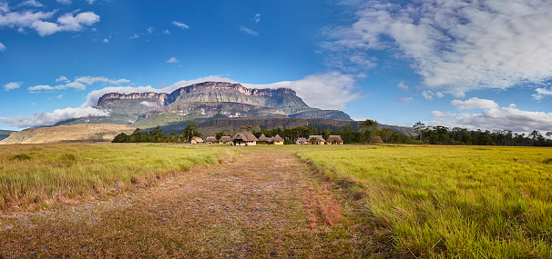 Lost World. Unique panoramic view of the Auyantepui (Auyan Tepuy) table top mountain at Uruyen indigenous tourist village. This beautiful and famous indigenous travel place is located south of the Auyantepui or AuyanTepuy in La Gran Sabana, Venezuela. La Gran Sabana, spreads into the regions of the Guiana Highlands and south-east into Bolívar State all the way to the borders with Brazil and Guyana. The largest National Park in Venezuela is Parima Tapirapecó located in the Amazon State. The Gran Sabana has an area of 10,820 km2 and is part of the second largest National Park in Venezuela, the Canaima National Park. The average temperature is around 20 °C , but at night can drop to 13 °C, nevertheless on top of the tepuis it can reach 0 °C (32 °F). La Gran Sabana shows one of the most unusual landscapes in the world, with rivers, waterfalls, deep and huge valleys, impenetrable jungles and savannahs that host large numbers and varieties of plant and animal species. The most prominent geological features are the table top mountains known as tepuis