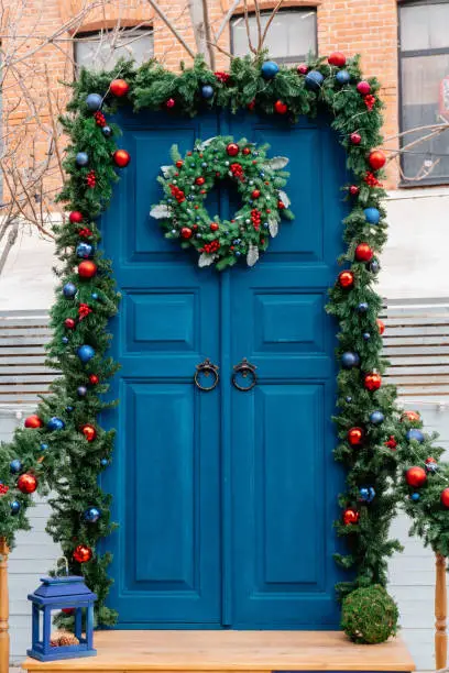 Photo of Entrance Christmas composition from a traditional Christmas wreath, arch of fir branches and railings decorated with fir branches