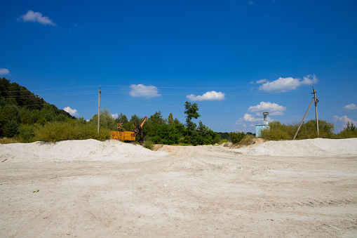 sandy and dusty polluted waste land environment space with not working industrial vehicle and forest background in clear weather day time with blue sky background
