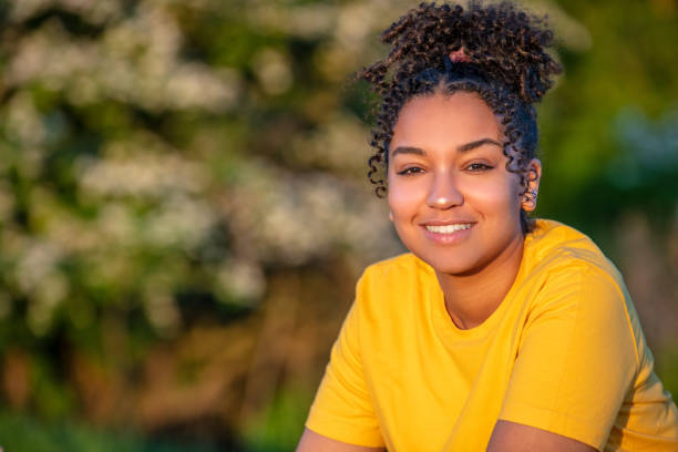 美しい人種混合人種アフリカ系アメリカ人ティーンエイジャーの十代の少女は、日没や日の出の外で完璧な歯で微笑んでいます - teenagers only ストックフォトと画像
