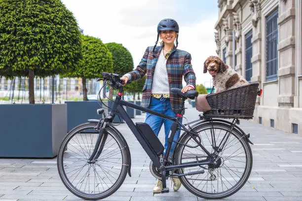 young woman pushing her electric bicycle with the dog in the basket