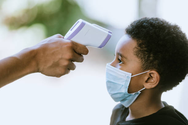 child with face mask has temperature taken at school - infrared thermometer imagens e fotografias de stock