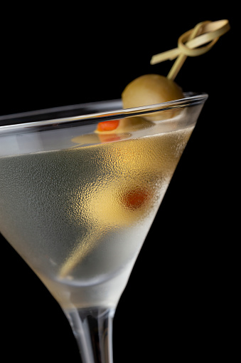 Macro detail of martini cocktail with vodka, dry gin, vermouth and some olives on a decorative wooden pick isolated on black background