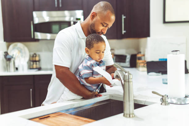 African American father helps his son wash his hands Adorable toddler boy dries his hands after washing them with dad’s help in the sink at home together paper towel stock pictures, royalty-free photos & images