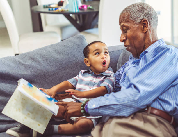 African American grandchild and grandfather read a book together at home Adorable toddler with his grandfather relaxing at home reading a book together preschool age photos stock pictures, royalty-free photos & images